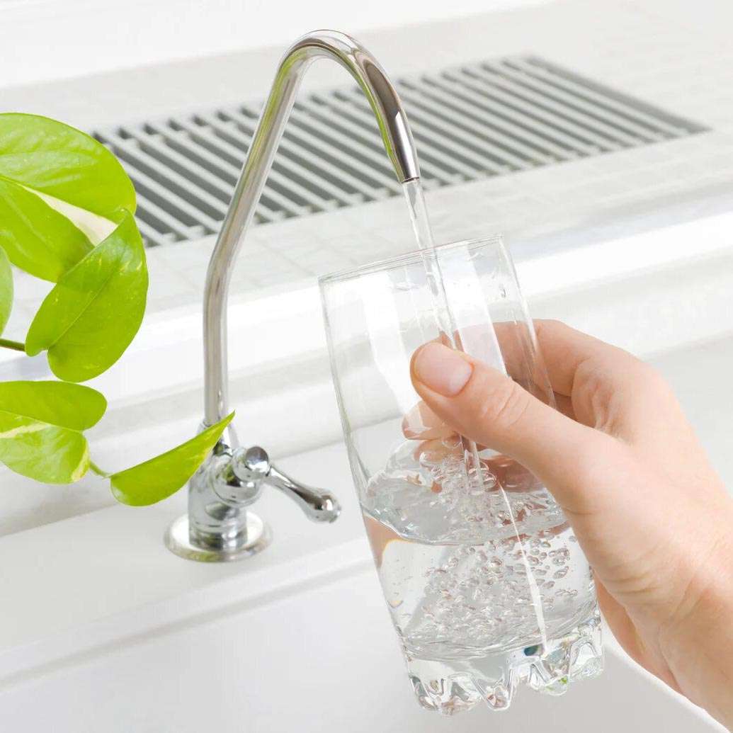 Mano sujetando un vaso llenándolo con agua filtrada por ósmosis desde un grifo especial de cocina.