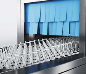 Lavavajillas de túnel industrial en inox con sistema de arrastre, con cortinilla azul y dispensorio blanco.