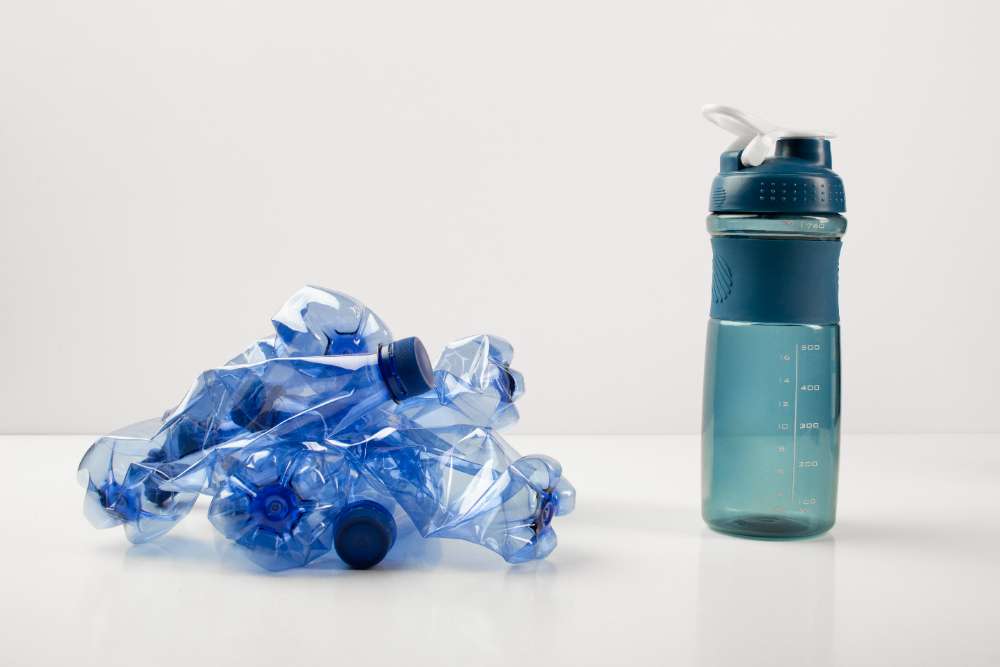Botellas de agua de plástico aplastadas en un lateral y en el otro un bidón de gimnasio transparente azulado relleno de agua.