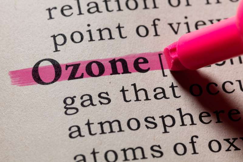 Primer plano de la palabra 'Ozone' en inglés resaltada en un diccionario con rotulador fosforescente rosa. Se pueden ver palabras clave descriptivas gas', 'atmósfera' y 'átomos'.
