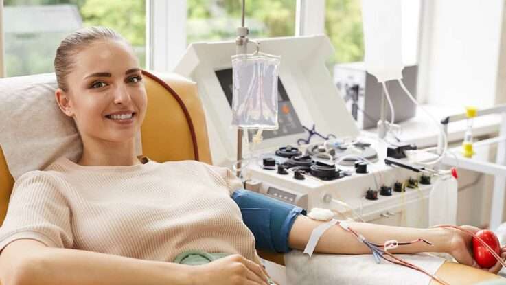 Imagen luminosa con mujer recostada en camilla sonriente, con tubos intravenosos, sujetando una bola de presión roja.