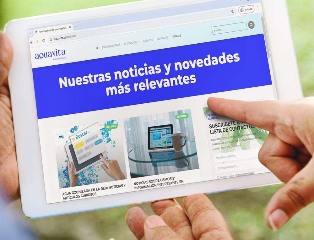 Primer plano de una tablet sujetada por dos manos y una tercera señalando la pantalla donde se ve la página de noticias de la web de AQUAVITA.