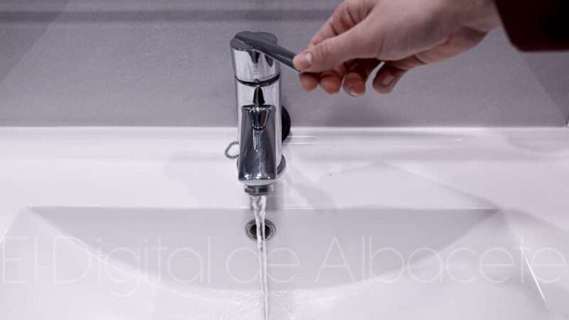 Una mano manipula un grifo de un lavamanos de donde sale agua.