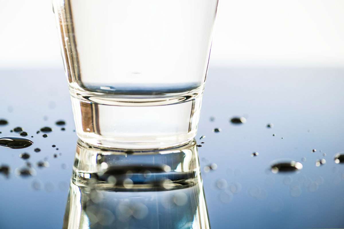 Primer plano de vaso de agua procesada por osmosis inversa sobre superficie con gotas alrededor