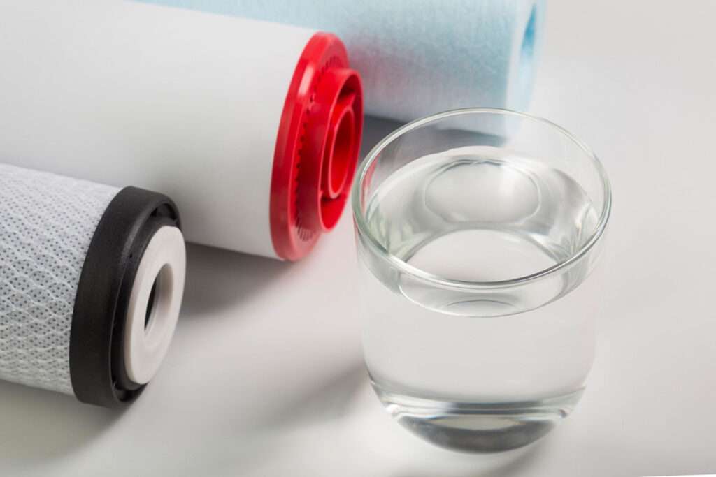 Tres tubos diferentes de filtrado por osmosis junto a un vaso lleno de agua