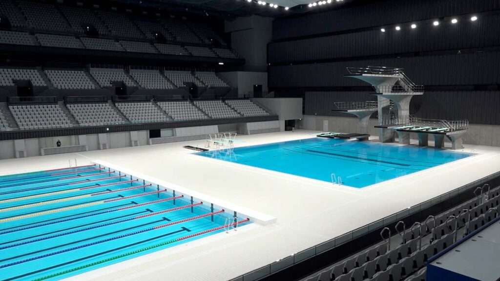 Vista panorámica de unas piscinas deportivas de competición y trampolines para saltos, al fondo se aprecian las gradas para el público